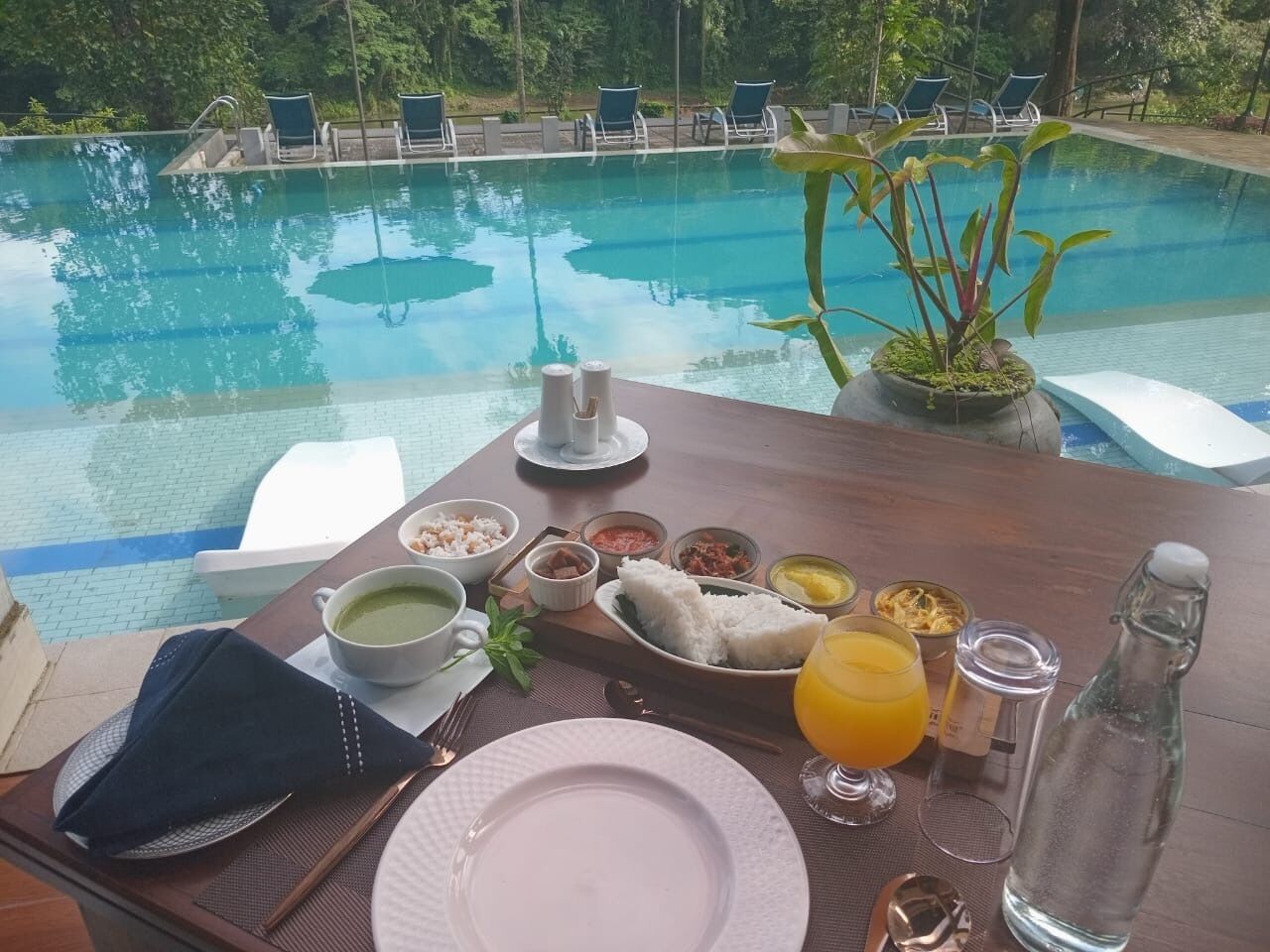 Ein Esstisch mit Mahlzeit am Pool, darunter Suppenschüsseln, Reis und ein Glas Orangensaft.