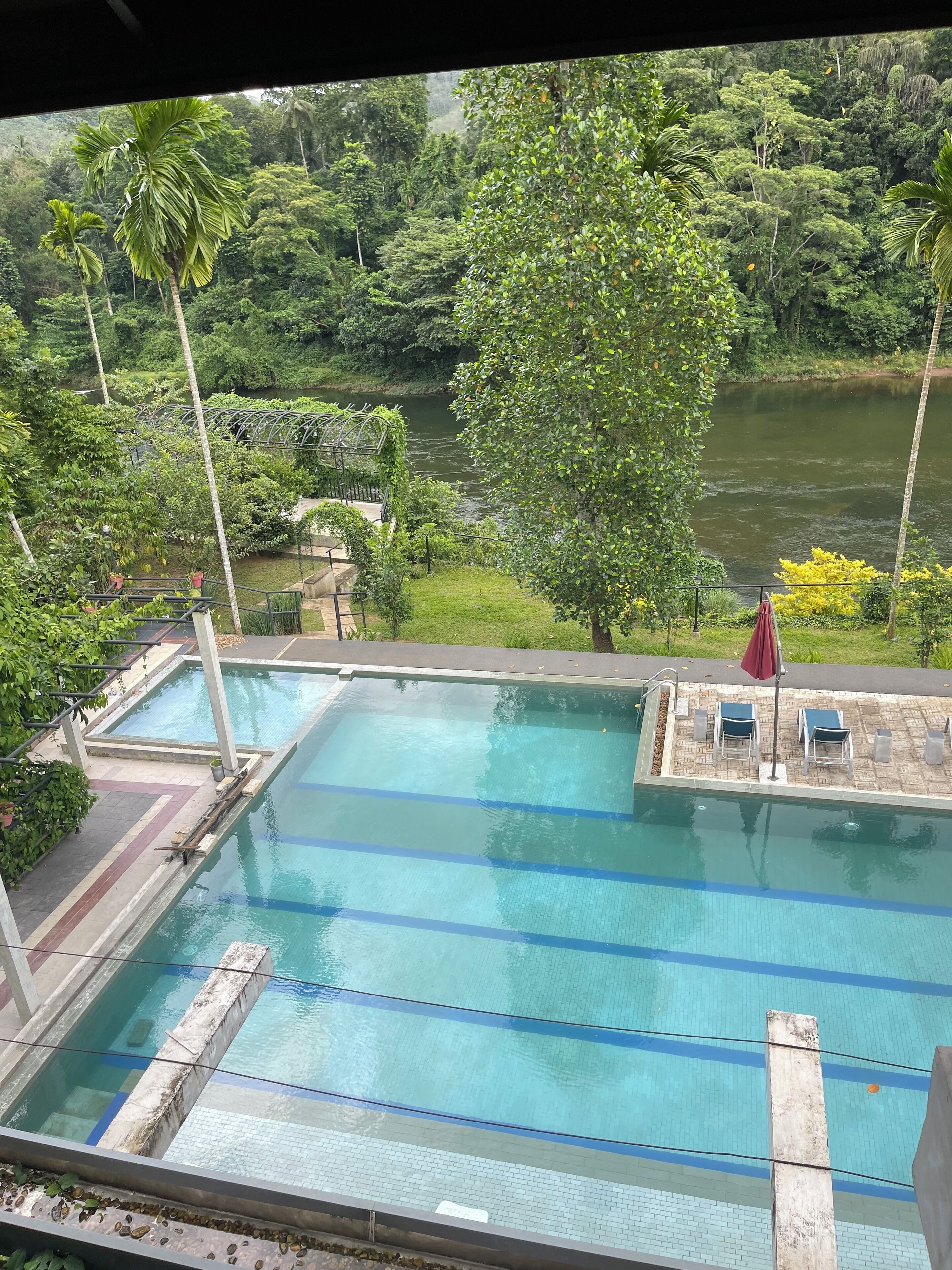Piscina com água azul cristalina, rodeada por vegetação exuberante e vista para um rio.