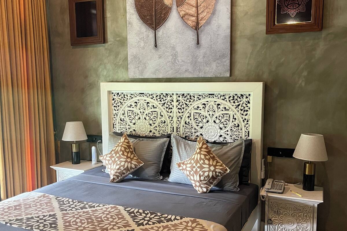 Une chambre à coucher avec un grand lit, deux tables de chevet, une tête de lit décorative et une œuvre d’art murale.