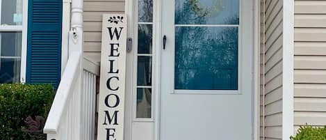 A front entrance with a 'WELCOME' sign, a mailbox, and a door with a wreath.