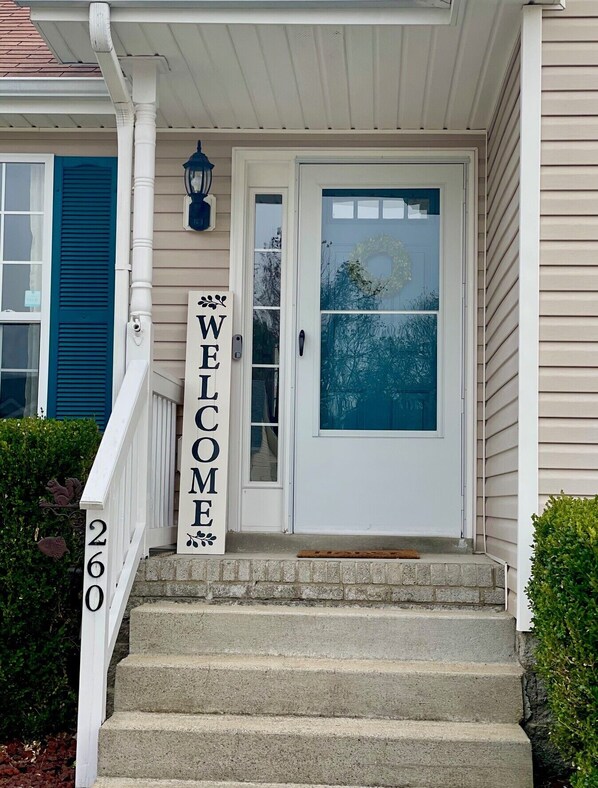 Una entrada principal con un letrero que dice 'WELCOME', un buzón y una puerta decorada con un adorno.