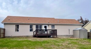 A single-story house with a front deck, a garage, and a small shed.