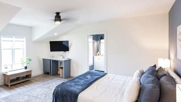 Een slaapkamer met een bed, nachtkastje, televisie en bureau met stoel.