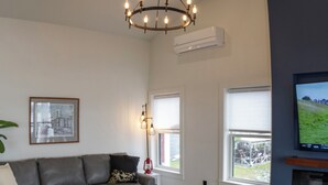 A modern living room with a grey sofa, a white coffee table, and a chandelier. - Captain Dan's Sunset Suite (St. Andrews)
