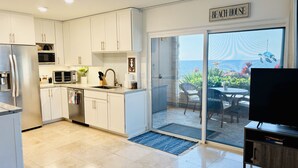 Une cuisine moderne avec des meubles blancs, un lave-vaisselle et une grande fenêtre donnant sur la mer.