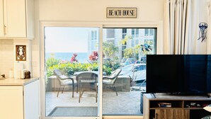 Un salon avec un téléviseur, un coin repas avec des chaises, un espace cuisine et une vue sur la mer et les bâtiments.