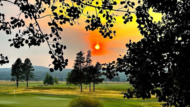 Campo de golf con atardecer, árboles y una bandera en el green.