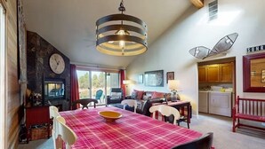 Un comedor acogedor con mantel a cuadros rojo, una lámpara colgante y una chimenea de piedra.
