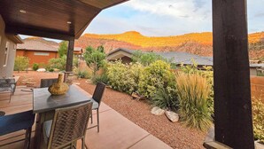 An outdoor patio area with a table and chairs, surrounded by a garden with various plants and a view of a hilly landscape. - Guest favorite near Zion/Epic view/Pickleball/Pool (Kanab)