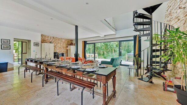 A spacious dining area with a long wooden table, benches, and a modern staircase.