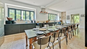 A spacious kitchen with dark cabinetry, a large island, and a dining area with a long table set for six.
