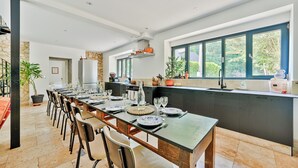 A modern kitchen with a long dining table, dark cabinetry, and a large window providing natural light.