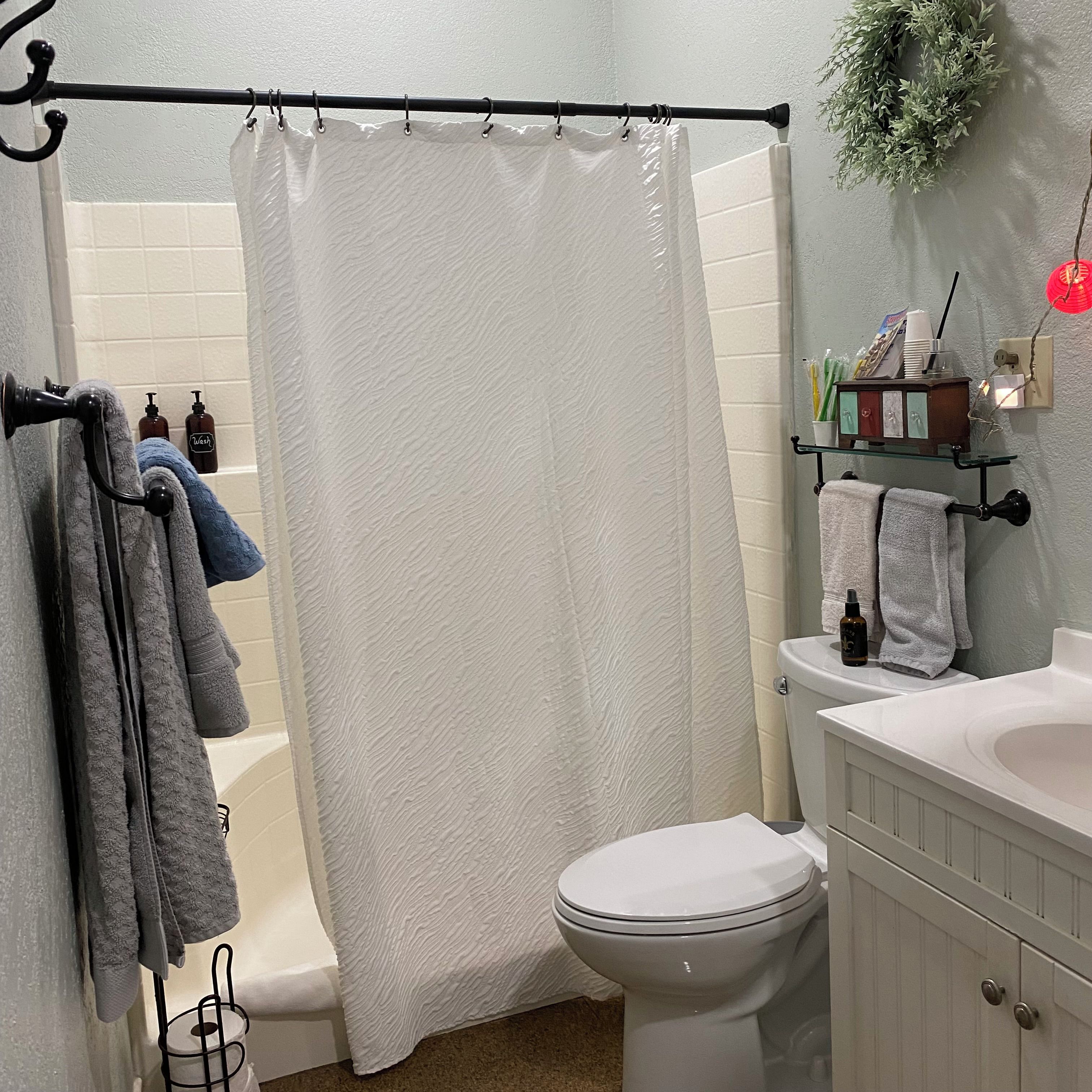 Un baño con cortina de ducha, inodoro, bañera y lavamanos con artículos de aseo.