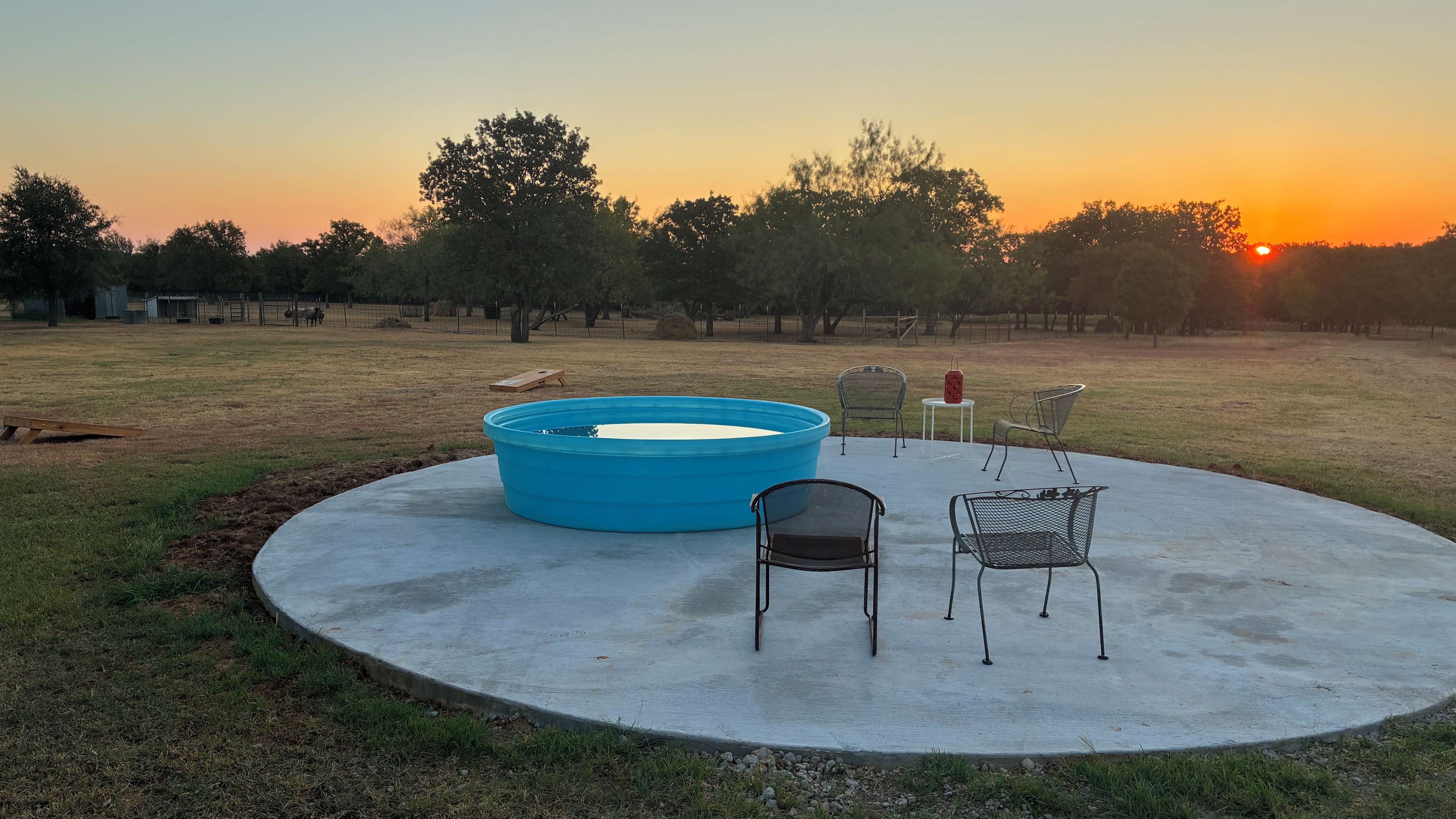 Eine Beton-Terrasse mit einem blauen Pool, zwei Metallstühlen und einem kleinen Tisch.