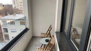 Un balcon avec une petite table et deux chaises en bois, une fenêtre et une vue sur les immeubles.