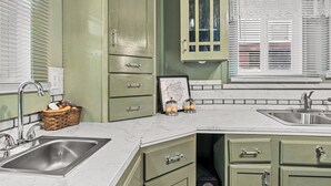 A kitchen with green cabinets, a marble countertop, and a window with blinds.