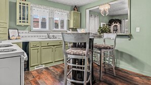 A kitchen with green cabinets, a white stove, and two bar stools with patterned cushions.