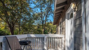 A covered patio with a grill, chairs, and a view of trees.