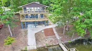Une maison en bois à deux étages, dotée d’une terrasse et d’un quai s’avançant dans un lac.