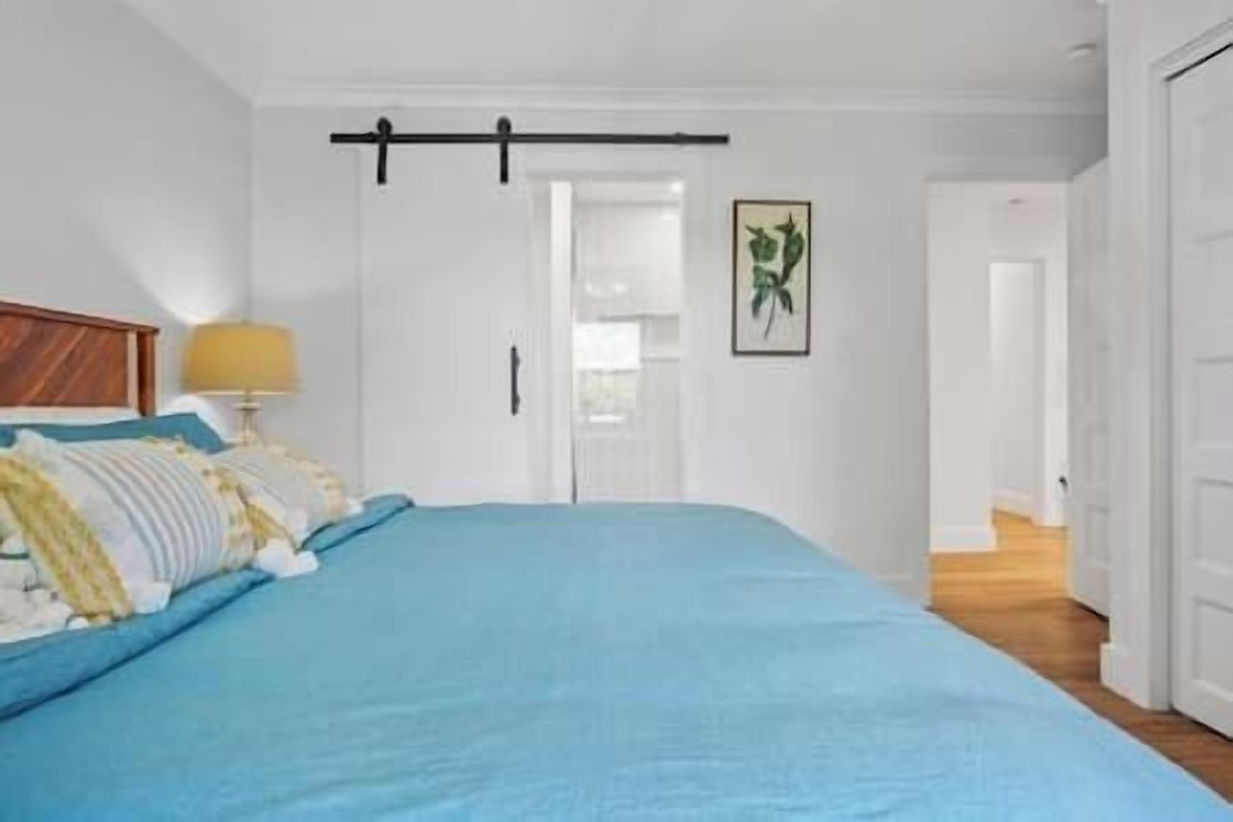 Quarto com cama, luminária de cabeceira, porta e quadro na parede.