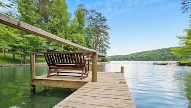 Une jetée en bois s’avançant dans un lac paisible, avec un banc placé sous une tonnelle en bois.