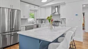 Une cuisine moderne dotée d’appareils électroménagers en acier inoxydable, de meubles blancs et d’un îlot central en marbre.
