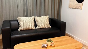 A living room with a black leather sofa, two beige pillows, a wooden coffee table with a small succulent plant, and a patterned rug. - Sol y Mar - Oceanfront Condo! (Cabo Rojo)