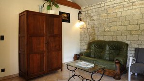 A living room with a stone wall, a green leather sofa, a wooden cabinet, and a glass coffee table. - Le Cellier aux Moines (COLOMBE LE SEC)