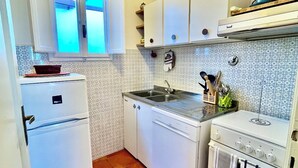 Une cuisine de taille réduite, dotée d’appareils électroménagers blancs, d’une fenêtre et d’un revêtement mural décoratif.