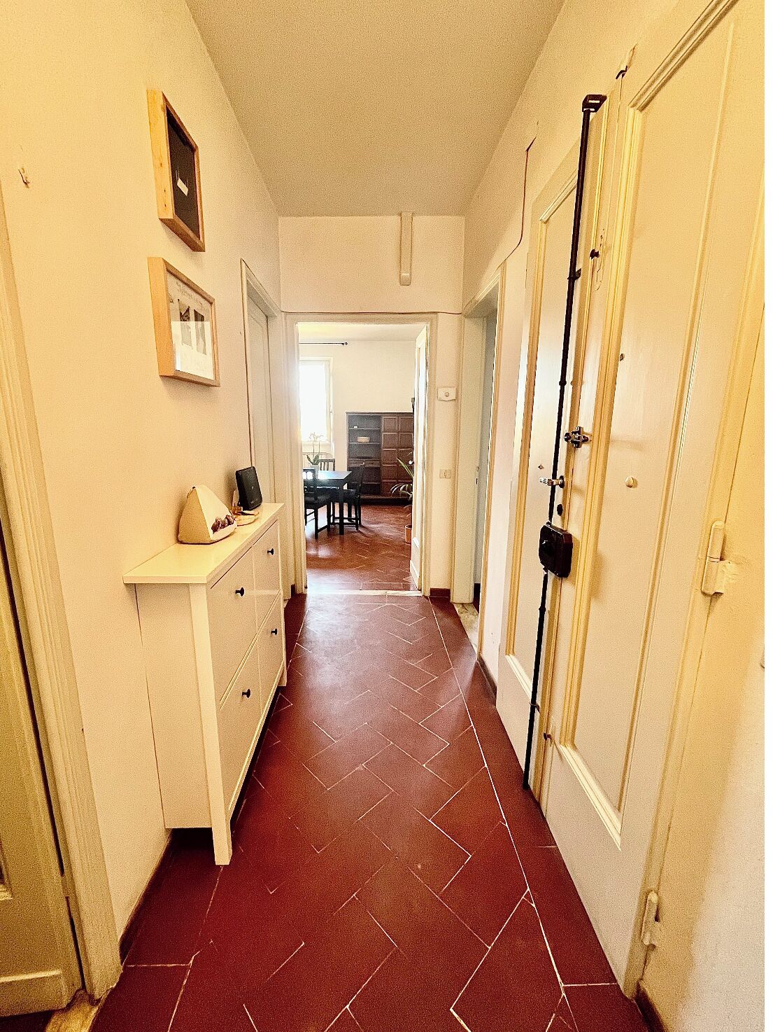 A hallway with a tiled floor, a white dresser, and a door with a black security device.