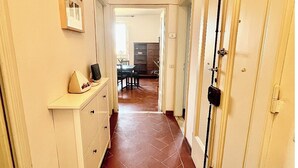 Un couloir avec un sol carrelé, une commode blanche et une porte équipée d’un dispositif de sécurité noir.