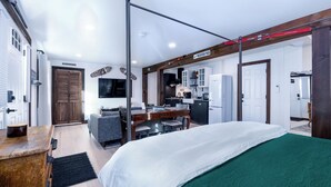A modern hotel room with a bed, a desk, and a kitchenette.