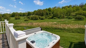A hot tub on a deck with a view of a grassy field and trees.