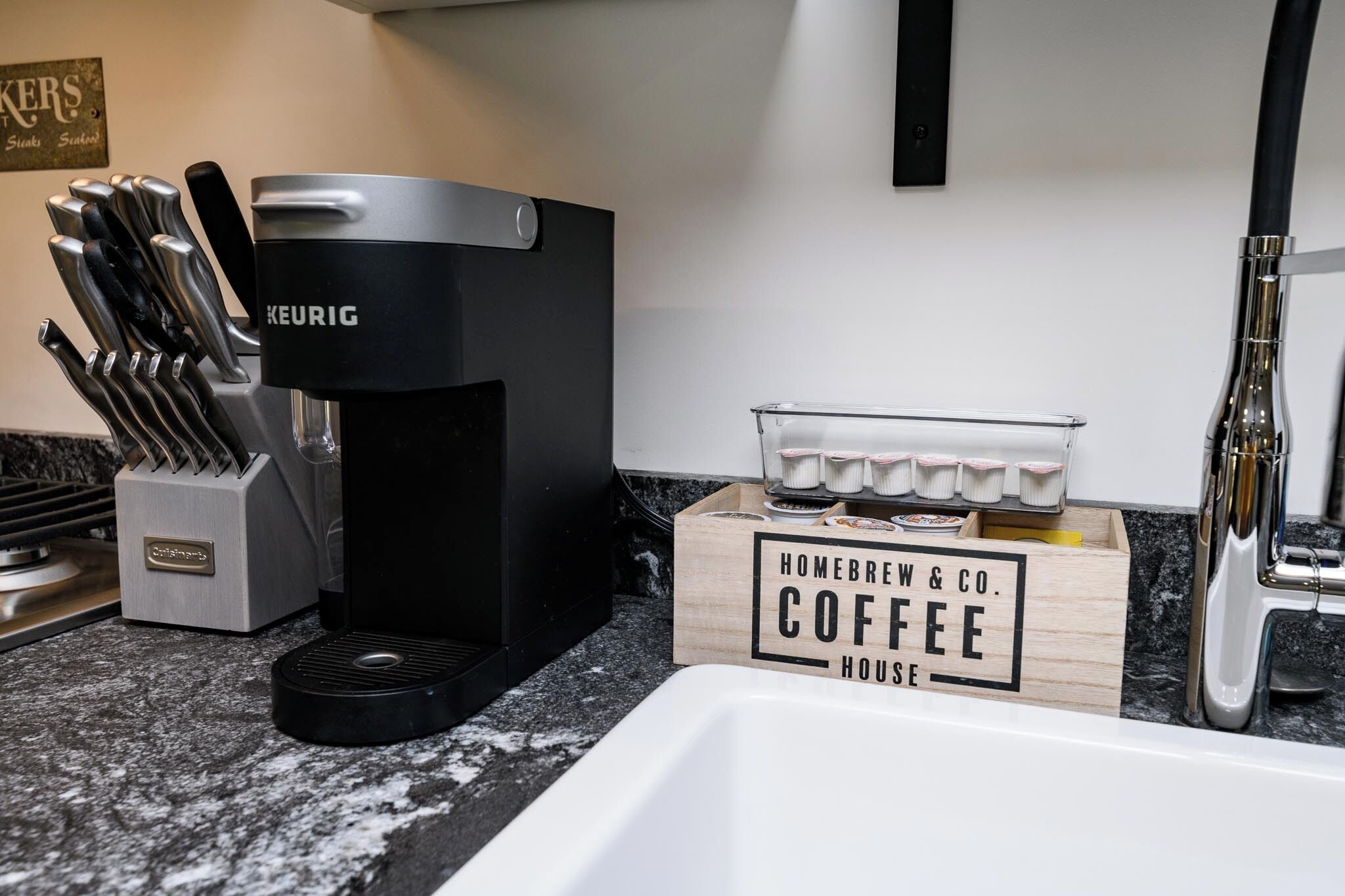 A kitchen with a Keurig coffee maker, a knife block, and a coffee service box labeled "Homebrew & Co. Coffee House".