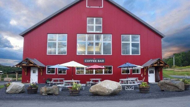 A red building with a sign that reads "Coffee Bar" and outdoor seating with umbrellas.
