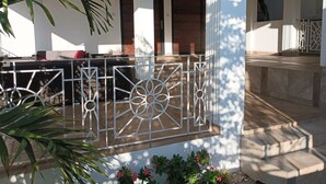 A covered outdoor seating area with a metal railing, potted plants, and a staircase leading to an upper level.