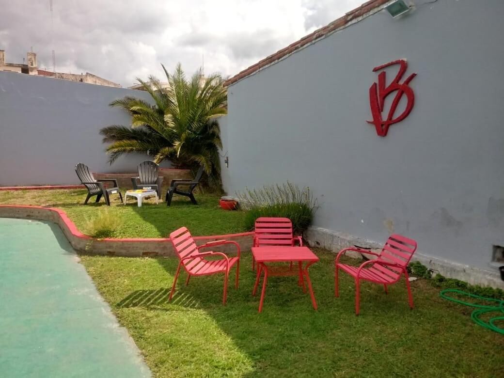 A pool area with red chairs and a table, a palm tree, and a wall with a red logo.
