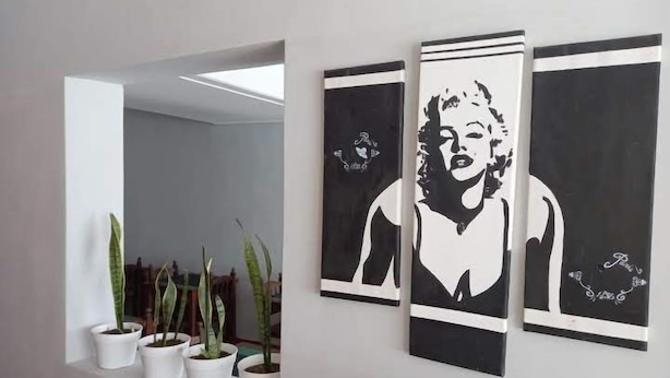 A hallway with three black and white framed artworks on the wall and several potted plants along the floor. - Buenavista Hotel (La Falda)
