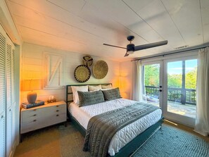 A bedroom with a bed, nightstands, a lamp, a ceiling fan, and a view through a sliding glass door.