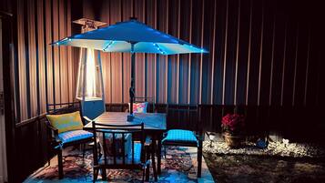 Een terras buiten met een tafel, stoelen, een blauwe parasol en een houten hek op de achtergrond.