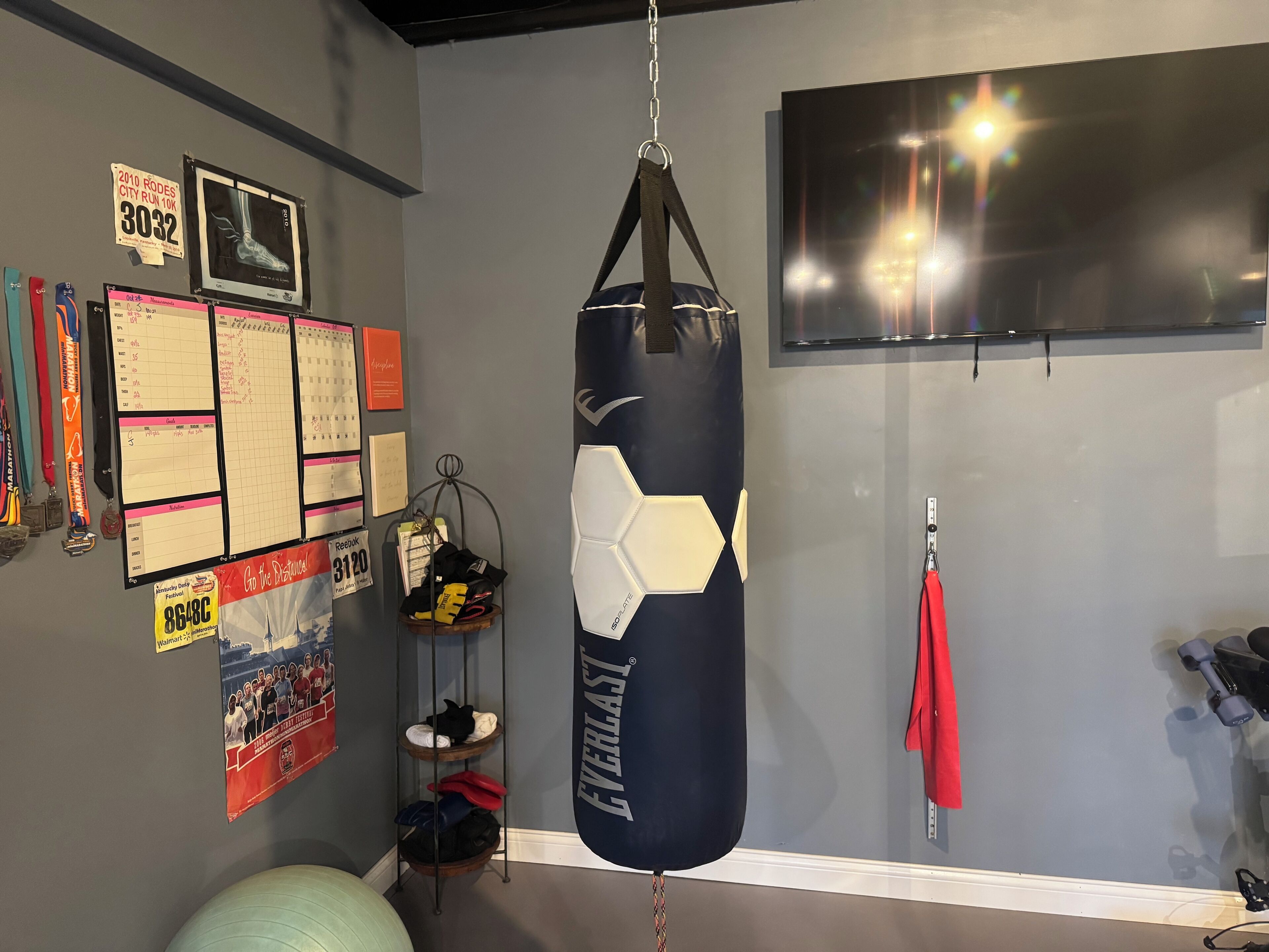A gym with a punching bag, a wall calendar, medals, and a TV.