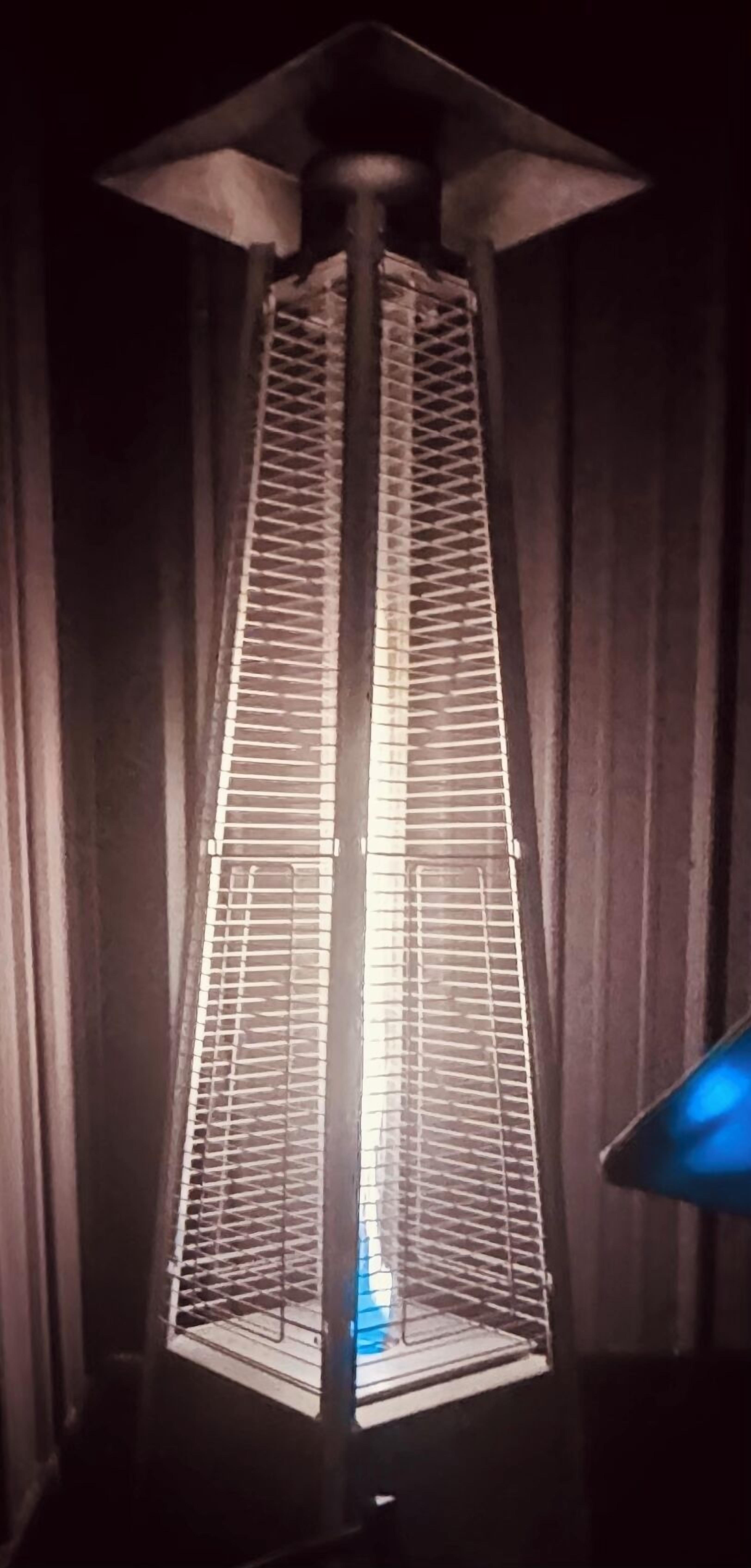 Uma luminária de chão alta e estreita, com estrutura de metal, base quadrada e cúpula cônica.
