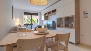 Een moderne keuken met witte kasten, een eettafel met stoelen, een televisie en een groot raam met gordijnen.