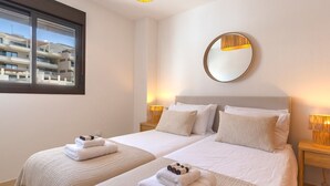 Een hotelkamer met twee bedden, een groot raam, een ronde spiegel en bedlampjes.