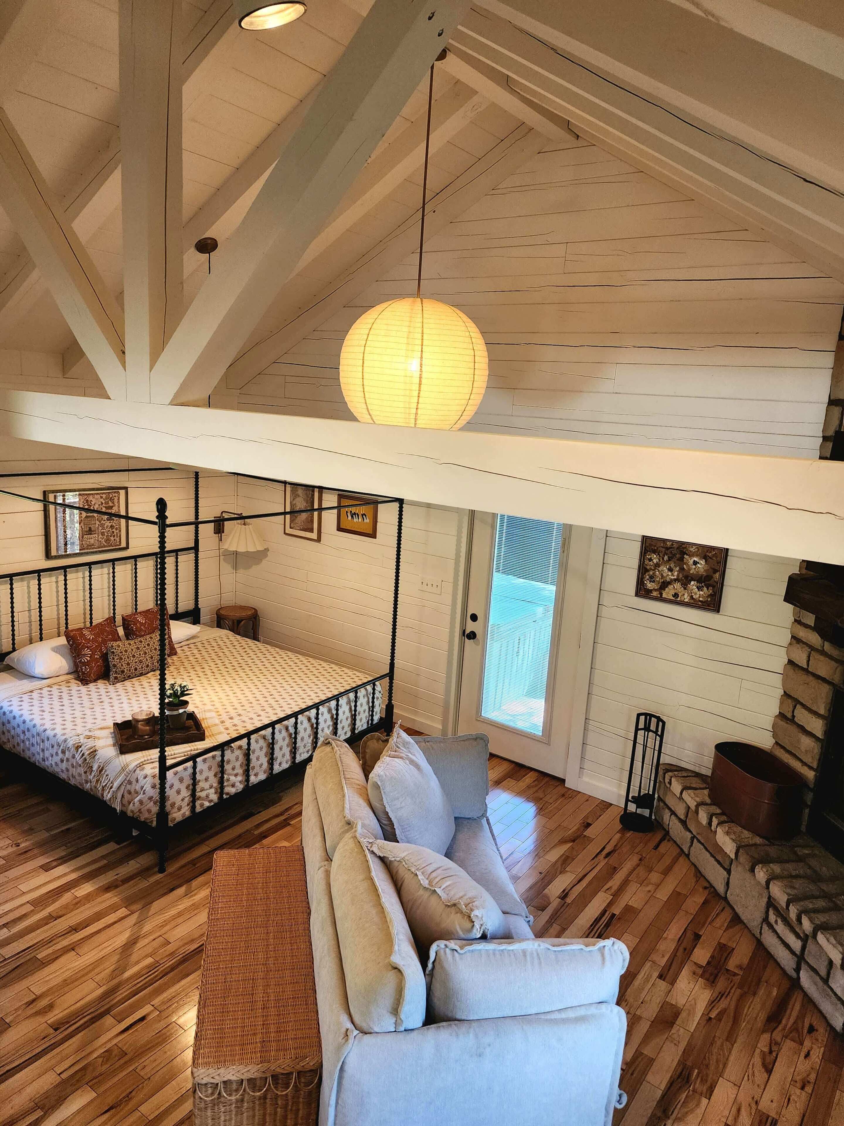A bedroom with a four-poster bed, a hanging light fixture, and a stone fireplace.