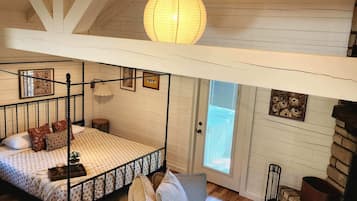 A bedroom with a four-poster bed, a hanging light fixture, and a stone fireplace.