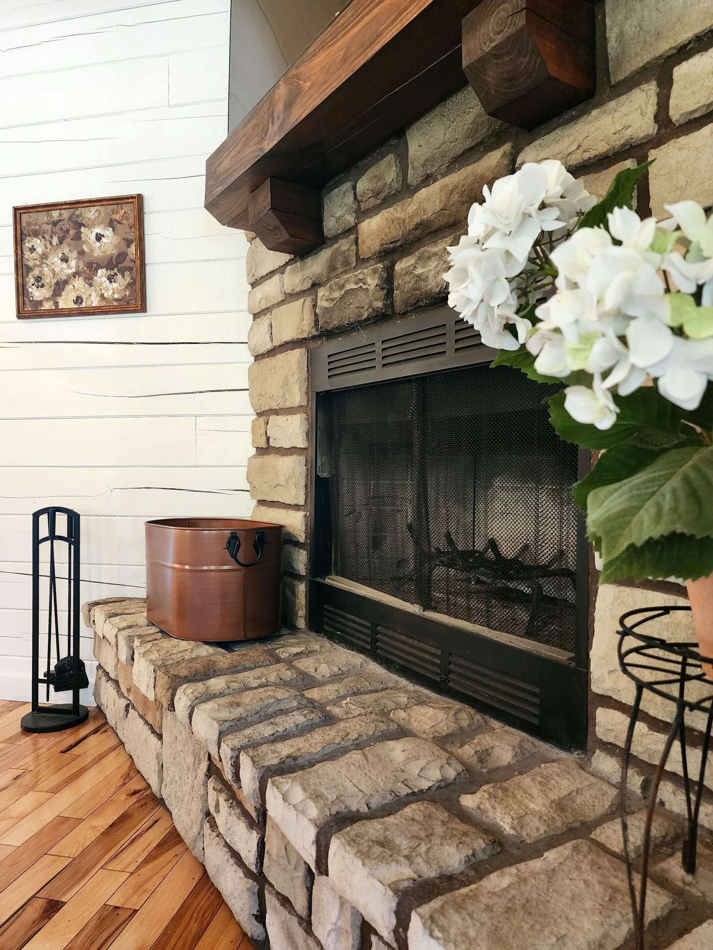 A stone fireplace with a screen, a copper pot, and a framed picture on the wall.