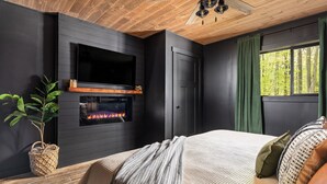 A modern bedroom with a fireplace, a ceiling fan, and a large window with curtains.