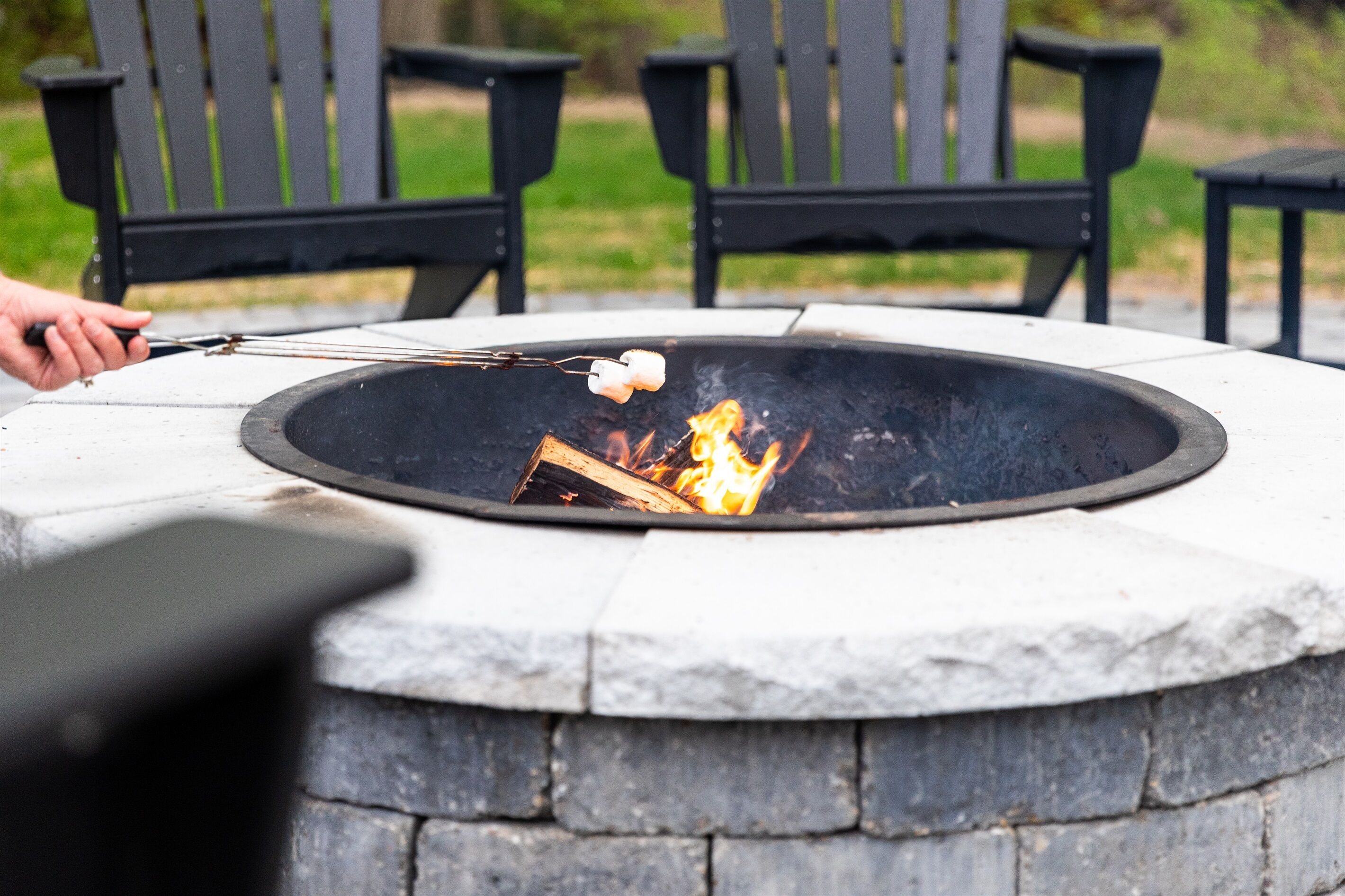 A stone fire pit with a fire burning, surrounded by black chairs.
