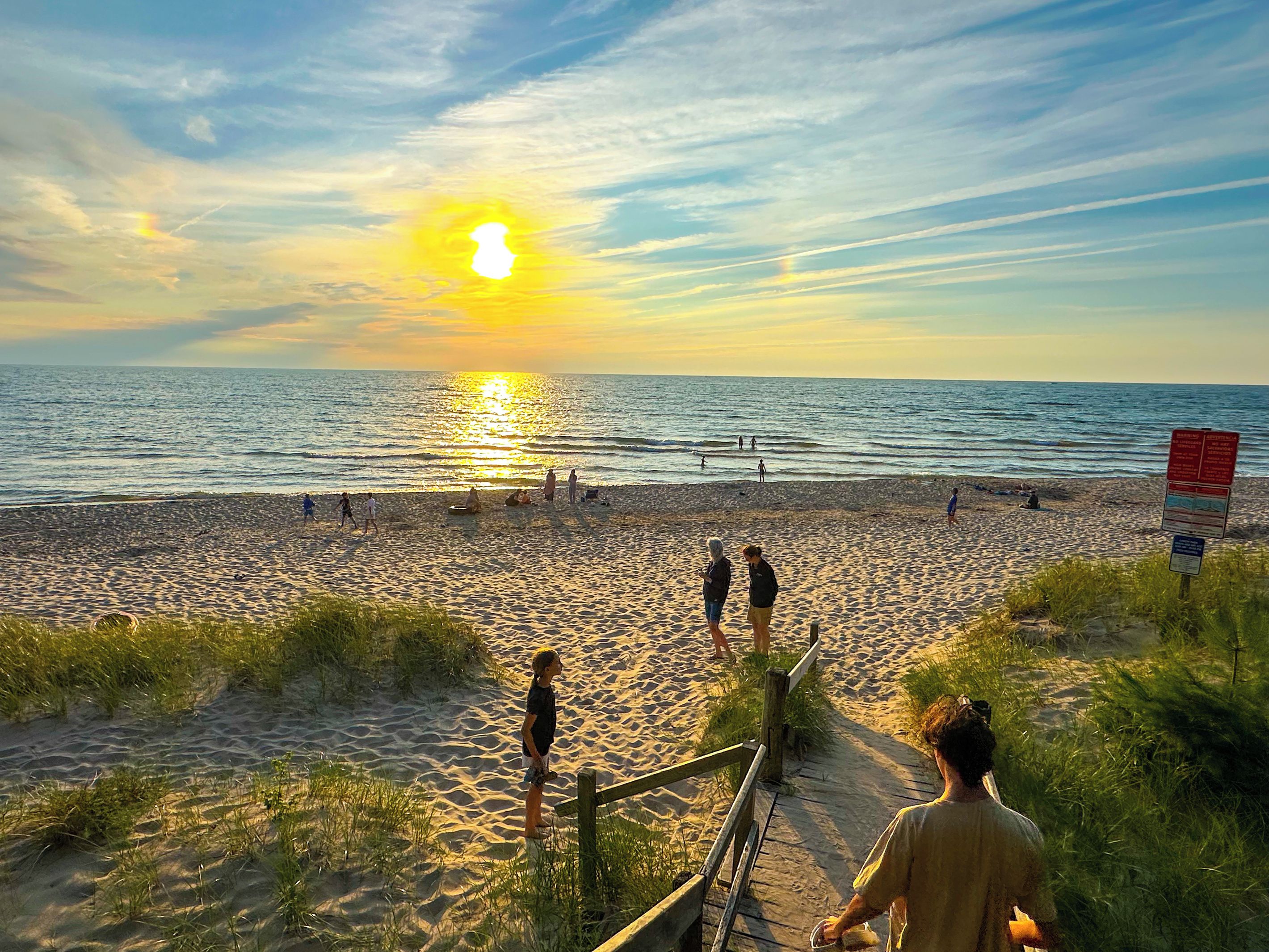 Een strand met een houten looppad dat naar het water leidt, een heldere lucht en de zon die onder de horizon verdwijnt.